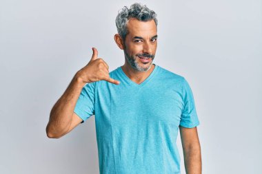 Orta yaşlı, gri saçlı, günlük kıyafetler giyen, gülümseyen, el ve parmaklarıyla telefonla konuşan bir adam. iletişim kavramları. 