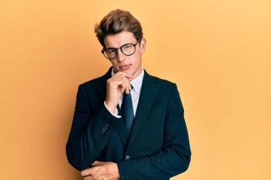 İş elbisesi ve kravat giyen yakışıklı beyaz adam kameraya kendinden emin bakıyor kolları çapraz ve çenesi açık gülümsüyor. Olumlu düşünmek. 