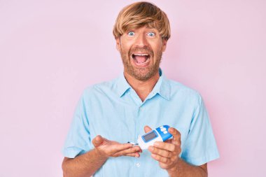 Genç sarışın adam glikoz ölçer kullanıyor. Çılgınlığı kutluyor ve başarıya hayret ediyor. Gözleri açık, heyecanlı çığlıklar atıyor.. 