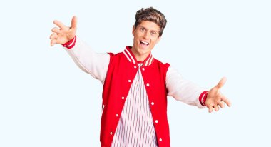 Beyzbol üniforması giyen yakışıklı bir adam kameraya bakıyor ve sarılmak için kollarını açmış gülümsüyor. Mutluluğu kucaklayan neşeli bir ifade.. 