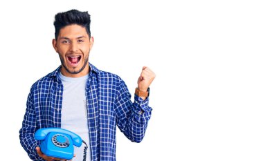 Yakışıklı Latin Amerikalı genç adam elinde klasik bir telefonla gururla bağırıyor zaferi ve başarıyı kutluyor. 