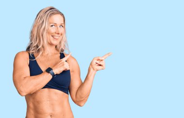 Orta yaşlı, formda, bikini giyen, gülümseyen ve kameraya bakan sarışın bir kadın.. 