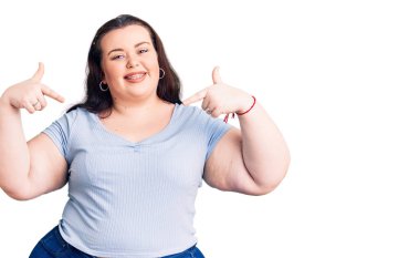 Genç ve cüsseli bir kadın gündelik kıyafetler giyiyor. Kendine güvenen, gülümseyen, kendini gururlu ve mutlu gösteren bir kadın.. 