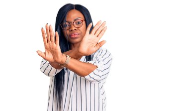 Genç Afrikalı Amerikalı kadın günlük kıyafetler ve gözlük takıyor. Reddedilme ifadesi. Kollarını kavuşturup negatif işaret veriyor, kızgın surat yapıyor. 