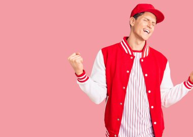 Beyzbol üniforması giyen yakışıklı genç adam çok mutlu ve heyecanlı, kollarını kaldırıp, gülümseyerek ve başarı için bağırarak kazanan jestler yapıyor. kutlama konsepti. 