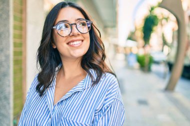 Genç İspanyol iş kadını şehirde mutlu bir şekilde yürürken gülümsüyor.