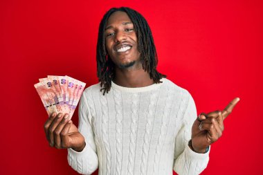 Afrika saçı örülü Afrikalı 50 rand 'lık banknotlar tutan Afro-Amerikalı adam mutlu bir şekilde elini ve parmağını yan tarafına uzatıyor. 