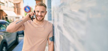 Genç İrlandalı gülümseyen mutlu bir adam şehrin caddesinde akıllı telefonda konuşuyor..