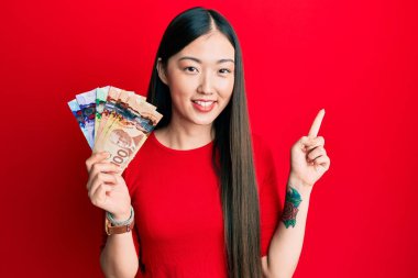 Kanadalı genç bir kadın elinde dolarlarla mutlu bir şekilde gülümsüyor. 