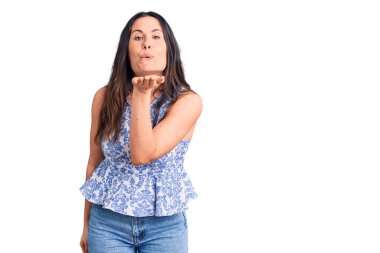 Genç, güzel, esmer, sıradan tişörtler giyen bir kadın kameraya bakıp havada bir öpücük savuruyor. Güzel ve seksi. aşk ifadesi. 