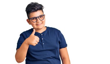 Gündelik kıyafetler ve gözlük takan küçük çocuk elleriyle mutlu bir jest yapıyor. Kameraya bakıp başarıyı gösteren ifade. 