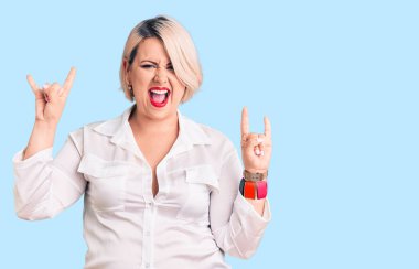 Genç, sarışın ve cüsseli bir kadın, gündelik tişört giyip çılgın bir ifadeyle bağırıyor, elleri havada rock sembolü yapıyor. Müzik yıldızı. ağır kavram. 