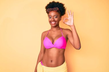 Genç Afro-Amerikan kadın bikini giyiyor, gülümsüyor ve el ve parmaklarıyla 
