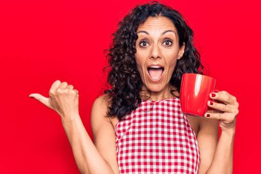 Orta yaşlı, güzel bir kadın, kahve fincanı içip parmağını yana doğru uzatarak mutlu bir şekilde gülümsüyor. 