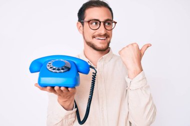 Kaliteli telefon tutan yakışıklı genç adam baş parmağını yana kaldırıyor ve ağzı açık gülümsüyor. 