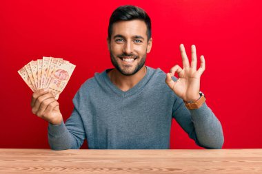 Yakışıklı İspanyol adam Meksika pezosu tutuyor. Parmaklarıyla imza atıyor, gülümsüyor. Mükemmel bir sembol. 