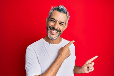 Orta yaşlı, beyaz tişört giyen, gülümseyen ve kameraya bakan gri saçlı bir adam.. 