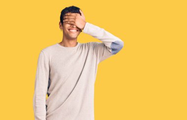 Gündelik giysiler giymiş genç Afro-Amerikan bir adam. Gülümsüyor ve elleri yüzüne gülüyor. Şaşırtmak için gözleri örtüyor. kör kavram. 