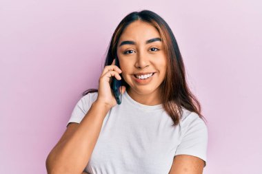 Genç Latin bir kadın akıllı telefondan konuşuyor. Olumlu ve mutlu görünüyor. Kendine güvenen bir gülümsemeyle dişlerini gösteriyor. 