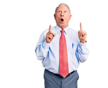 Zarif kravat ve gömlek giyen yaşlı, beyaz saçlı adam şaşırmış ve şaşırmış bir şekilde yukarı bakıyor ve parmaklarıyla işaret ediyor ve kollarını kaldırıyor.. 