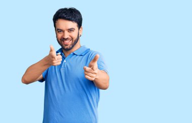 Günlük kıyafetler giyen genç İspanyol adam mutlu ve komik yüzüyle kamerayı işaret ediyor. iyi enerji ve titreşimler. 