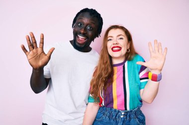 Irklar arası çift gündelik kıyafetler giyer ve parmaklarını on numarayla göstererek mutlu ve kendinden emin bir şekilde gülümserler.. 