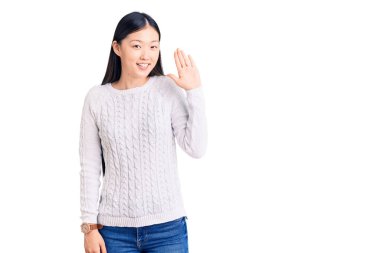 Genç, güzel, Çinli bir kadın gündelik bir süveter giyip merhaba diyor mutlu ve gülümsüyor, dostça bir hoş geldin jesti. 