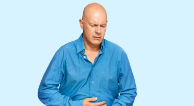 Orta yaşlı kel bir adam elleri karnında günlük kıyafetler giyiyor çünkü hazımsızlık, acı verici bir hastalık kendini iyi hissetmiyor. Ağrı kavramı. 