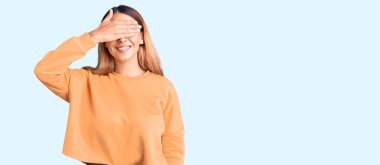 Gündelik kıyafetler giyen, gülümseyen ve gülümseyen güzel genç bir kadın şaşırtmak için gözlerini kapatıyor. kör kavram. 