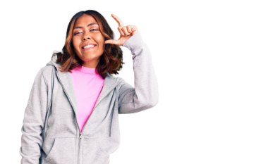 Genç, güzel, melez, sportif kıyafetler giyen, gülümseyen, kendine güvenen, el hareketi yapan, parmaklarıyla işaret yapan ve kameraya bakan bir kadın. ölçüm kavramı. 