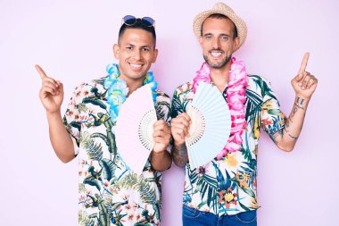 Yazlık tişört giyen iki genç gay el ele tutuşup gülümsüyor. 