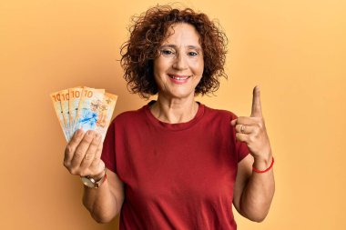 Güzel orta yaşlı bir kadın elinde 10 İsviçre frankı banknotuyla gülümsüyor bir fikir veya soru işareti ile mutlu bir yüzle, bir numara 