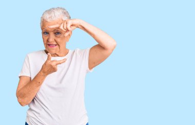 Mavi gözlü, gri saçlı, sıradan beyaz tişörtlü, gülümseyen, elleri ve parmakları mutlu yüzlü son sınıf güzeli kadın. yaratıcılık ve fotoğrafçılık kavramı. 