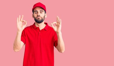 Sakallı, teslimat üniforması giyen, gözleri kapalı gülümseyen ve parmaklarıyla meditasyon yapan yakışıklı bir genç. yoga konsepti. 