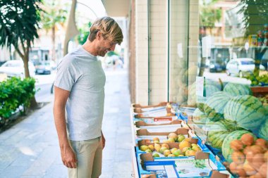 Genç İrlandalı gülümseyen mutlu bir adam markette meyveye bakıyor..