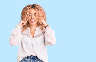 Kıvırcık saçlı, zarif yaz gömleği giyen, kulaklarını parmaklarıyla kapatan, gürültülü müzik sesi için rahatsız edici ifadeleri olan genç sarışın kadın. sağır kavramı. 