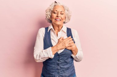 Yaşlı, gri saçlı, sıradan kıyafetler giyen, elleri göğsünde gülümseyen, gözleri kapalı, yüzünde minnet ifadesi olan bir kadın. sağlık kavramı. 