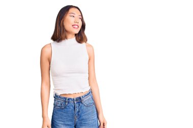 Genç, güzel Çinli bir kız, günlük kıyafetler giyip, yüzünde gülümsemeyle yan yana bakıyor, doğal bir ifade. Kendinden emin gülen. 