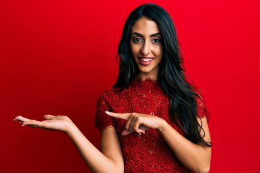 Kırmızı arka planda zarif kıyafetler giyen güzel İspanyol kadın kameraya hayret ediyor ve gülümsüyor.. 