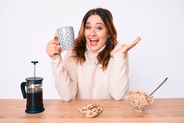 Masada oturan güzel beyaz bir kadın zaferi kutluyor. Gülümsüyor ve ellerini kaldırarak kazanan ifadesini takınıyor. 