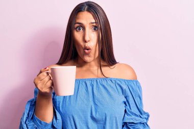 Genç, güzel esmer kadın bir kupa kahve içiyor. Korkmuş ve şaşkına dönmüş bir şekilde ağzı açık şaşkınlık içinde, inançsız bir yüz. 