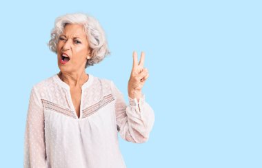 Gri saçlı, sıradan kıyafetler giyen, kameraya gülümseyen ve zafer işareti yapan yaşlı bir kadın. İki numara.. 