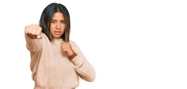 Kışın yün kazak giyen genç Latin kız dövüşmek için yumruk atıyor, agresif ve öfkeli saldırı, tehdit ve şiddet 