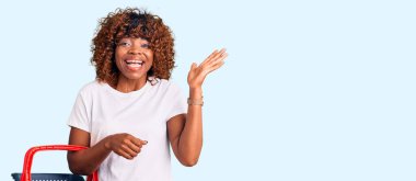 Genç Afro-Amerikalı kadın elinde süpermarket alışveriş sepeti tutarak zaferi mutlu bir gülümseme ve ellerini kaldırarak kazanan ifadeyle kutluyor. 