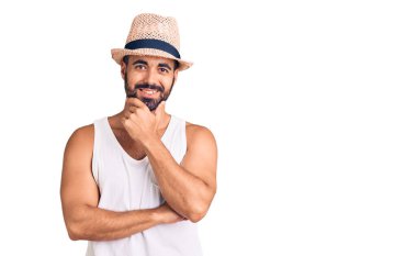 Gündelik yaz şapkası takan genç İspanyol adam kameraya bakarken kollarını kavuşturup gülümsüyor ve çenesini kaldırıyor. Olumlu düşünmek. 