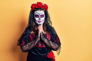 Ölü kostümünü giyip sarıya bürünmüş genç bir kadın elleriyle dua ediyor ve af diliyor kendinden emin bir şekilde gülümseyerek.. 