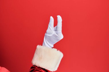 Elinde Noel Baba kostümü ve kırmızı arka plan eldivenleri olan görünmez bir şey tutan, parmakları yer gösteren bir adam. 