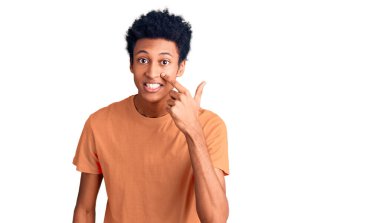 Genç Afro-Amerikan adam, günlük kıyafetler giyip, el ve burunla işaret ederek, neşeyle gülümsüyor. güzellik konsepti 