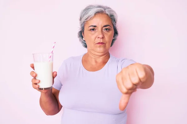 年长的惊慌失措的女人满脸怒容地捧着一杯牛奶 消极的迹象表明她不喜欢大拇指朝下 拒绝的观念 — 图库照片