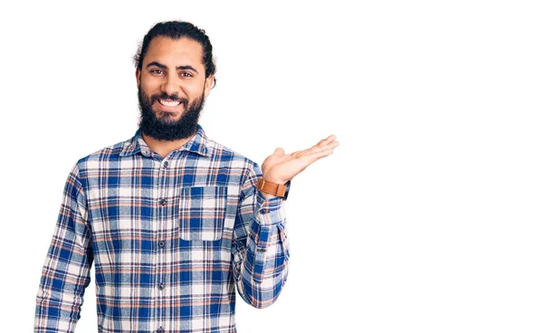 若いですアラブ人男身に着けているカジュアル服笑顔陽気なプレゼンテーションとポインティングで手の手のひらカメラを見て — ストック写真